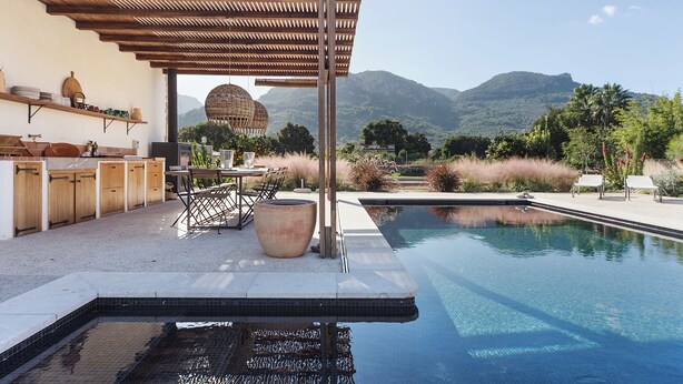 A poolside area with a pergola, outdoor seating, and a view of mountains.