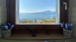 A window with a view of a lake and mountains, a balcony with potted plants, and a door with a handle. - Villa I Gelsomini,  6 Bedrooms, Garden, Terrace, Stunning View of Lake Garda (TORRI DEL BENACO - VENETO)