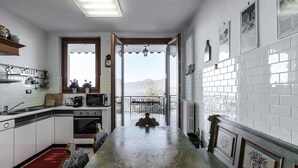 A kitchen with white cabinets, a large island, and a view of the mountains through an open door. - Villa I Gelsomini,  6 Bedrooms, Garden, Terrace, Stunning View of Lake Garda (TORRI DEL BENACO - VENETO)