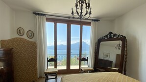 A bedroom with a large bed, a wooden dresser, a chair, a mirror, and a view of the sea through a sliding door. - Villa I Gelsomini,  6 Bedrooms, Garden, Terrace, Stunning View of Lake Garda (TORRI DEL BENACO - VENETO)
