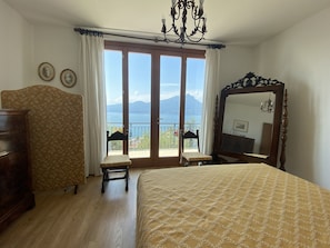 Una camera da letto con un letto grande, una cassettiera in legno, una sedia, uno specchio e vista mare tramite una porta scorrevole.