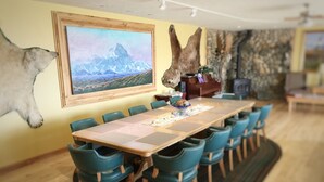A dining area with a long table, teal chairs, a mounted animal head, and a mountain landscape painting on the wall. - Pioneer Ridge B&B Inn (Wasilla)