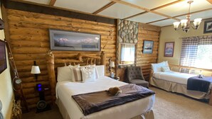 A log cabin bedroom with a large bed, a smaller bed, a sofa, a mounted TV, and a stone wall. - Pioneer Ridge B&B Inn (Wasilla)