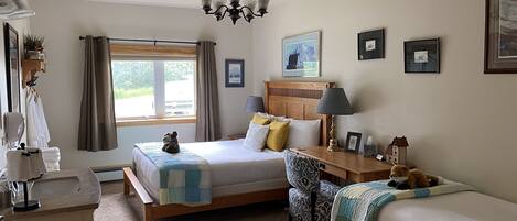 A well-lit bedroom with a large bed, bedside tables, a chair, and a window with curtains.
