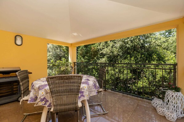 Un patio couvert avec une table et des chaises, un barbecue et une vue sur une végétation luxuriante.