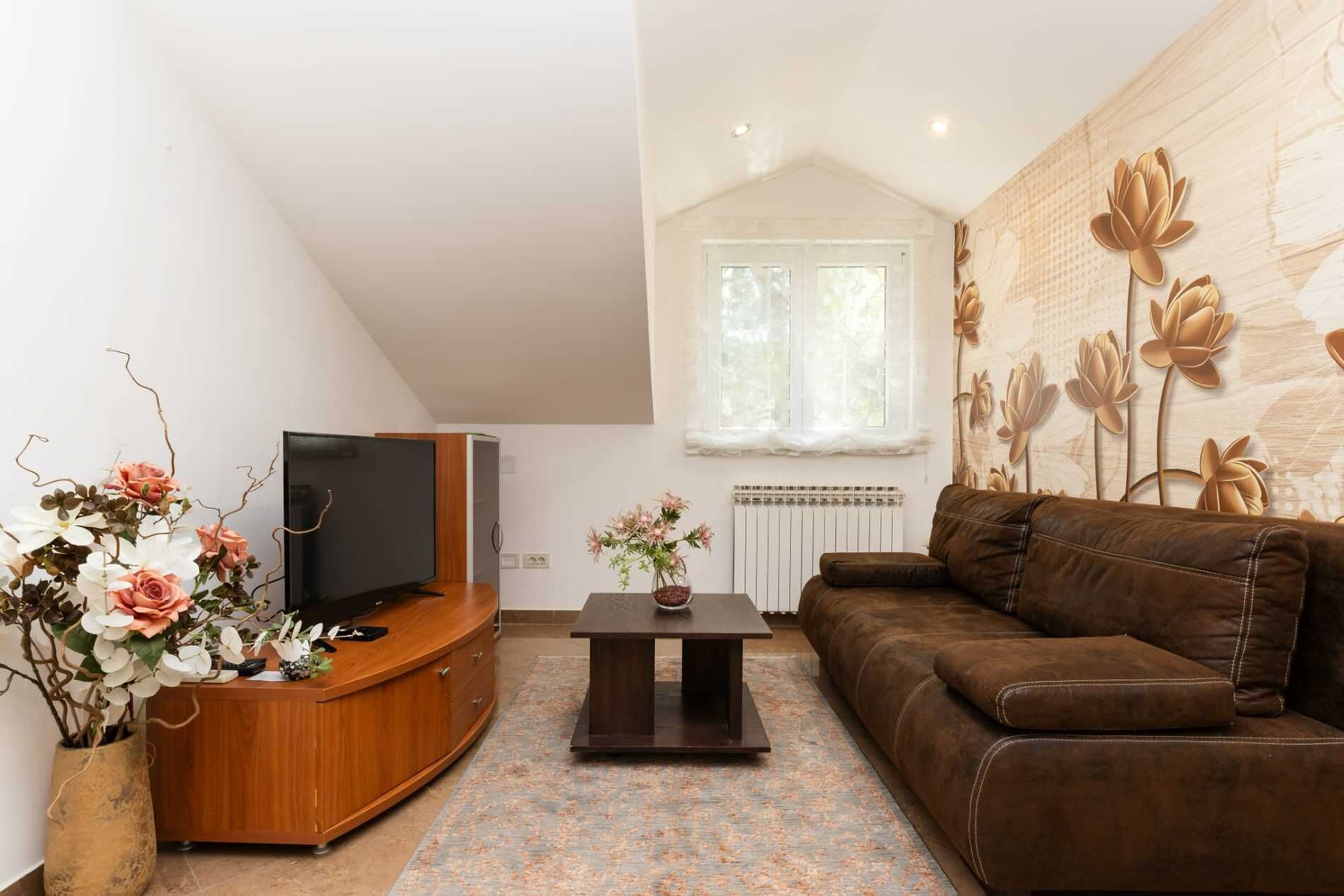 Uma sala de estar com televisão, sofá, mesa de centro e plantas decorativas.
