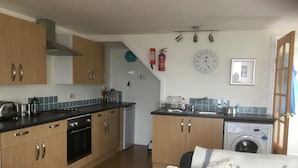 A compact kitchen with wooden cabinets, a stove, a washing machine, and a sink.
