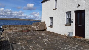 A white building with a stone-paved courtyard, a wooden door, and a view of the sea.