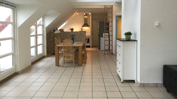 A modern kitchen with a dining area, featuring a wooden table and chairs, a white cabinet, and a view through a window. - Holiday home with beautiful sea views. (Frørup)