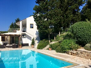A two-story building with a pool, outdoor furniture, and a staircase leading to a balcony.