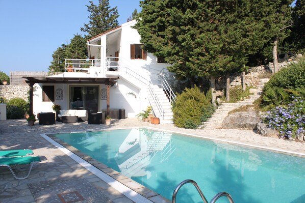 A pool area with a white building, outdoor seating, and a staircase leading up to the building.