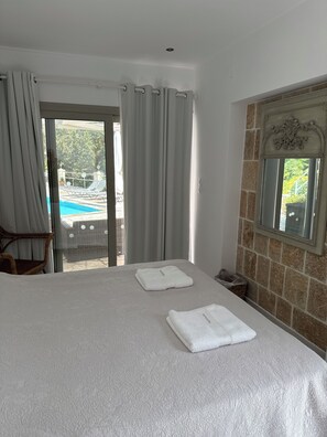 Habitación de hotel con cama, una silla, ventana con vista a una piscina y un espejo en la pared.