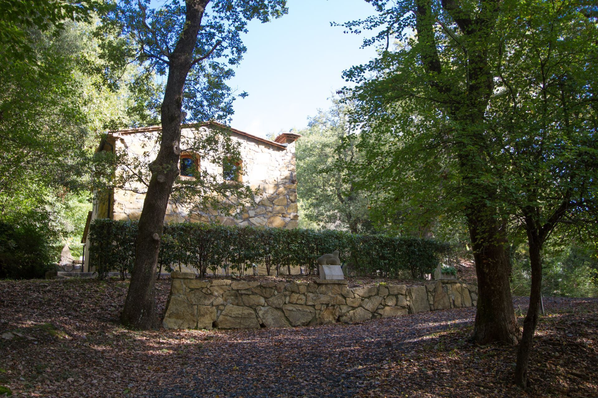 Edifici de pedra amb teulada de rajola, envoltat d'arbres i una paret de pedra.