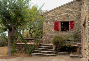 A stone house with a wooden staircase leading to a window with red shutters.