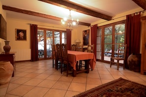 A dining area with a table set for four, wooden chairs, a chandelier, and large windows with curtains.