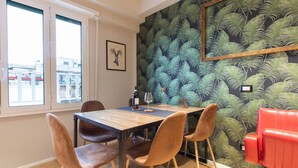 Ein Essbereich mit einem Holztisch, vier Stühlen, einer rot gepolsterten Bank, einem gerahmten Bild an der Wand und einer Wandtapete mit Muster.