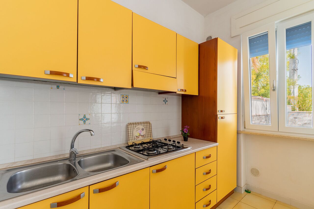 Een keuken met gele kastjes, een roestvrijstalen gootsteen en een gasfornuis.