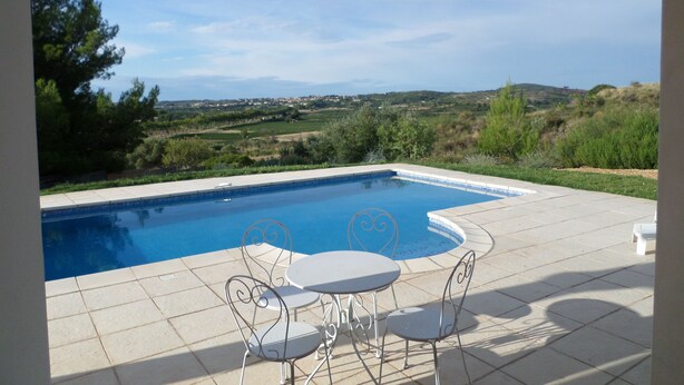 Une piscine avec vue sur la campagne, entourée d’un sol carrelé et de chaises en métal.
