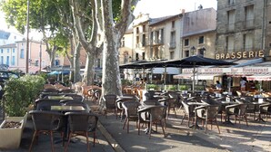 Espace extérieur aménagé avec des chaises et des tables en osier, un café doté de parasols et un bâtiment arborant une enseigne indiquant la présence d’un restaurant.