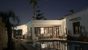 Un espace piscine doté d’une terrasse, de palmiers et d’un bâtiment aux grandes fenêtres.