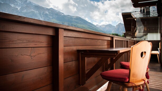 A wooden deck with a table and chairs, overlooking a mountainous landscape.