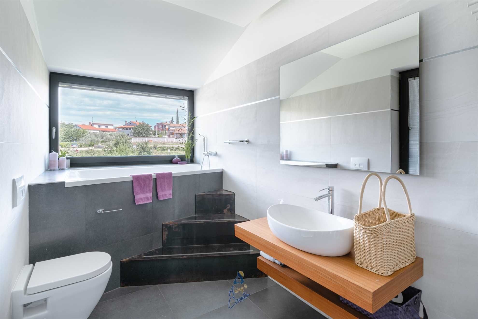 A modern bathroom with a large window, a white sink, and a mirror.