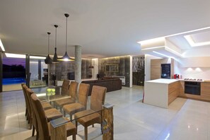 A modern interior with a glass dining table, leather chairs, pendant lighting, a kitchen with a built-in oven, and a view of a swimming pool. - Vibrant modern 5-BR Villa for 10+2, with pool and a sea view (Višnjan)