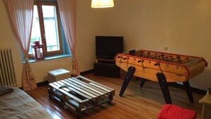 A cozy room with a wooden futsal table, a futsal table, a sofa, a television, and a window with curtains. - Rental apartment type 2 in mountain house in Risoul - 05600 (Risoul)
