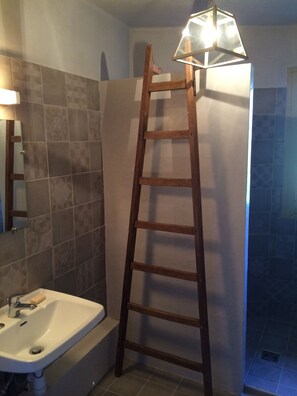A bathroom with a wooden ladder leaning against a tiled wall, a sink, and a mirror.