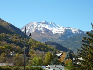 A mountain with a snow-capped peak, surrounded by forested hills and a few buildings.