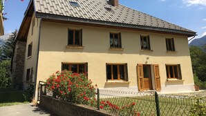 A two-story house with a sloped roof, multiple windows, and a wooden door. - Rental apartment type 2 in mountain house in Risoul - 05600 (Risoul)