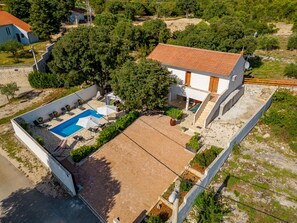 An aerial view of a residential property with a swimming pool, a patio area, and a garden.