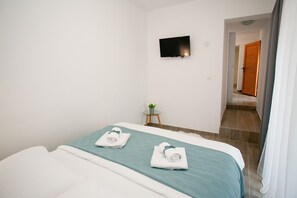 Een hotelkamer met een bed, een aan de muur bevestigde televisie en een klein tafeltje met een plant.