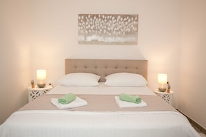 A neatly made double bed with two pillows, two bedside tables with lamps, and a wall art piece above the bed.