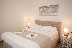 A neatly made bed with two pillows, a green towel, and a beige bedspread. There is a wall-mounted artwork above the bed and two bedside tables with lamps.
