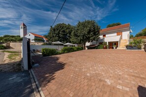 A spacious courtyard with a paved walkway, a church with a bell tower, and a modern house with a red-tiled roof.