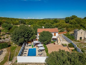 A villa with a swimming pool, surrounded by lush greenery and a stone building.