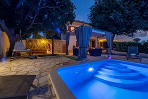 Ein Poolbereich im Freien mit einer Steinterrasse, einem Whirlpool und einer überdachten Sitzgelegenheit.
