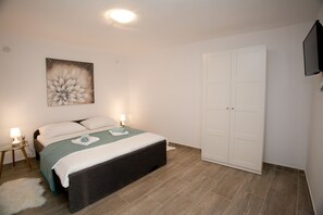 Ein Schlafzimmer mit einem Bett, Nachttischen, einem Gemälde, einem Kleiderschrank und einem Fernseher.