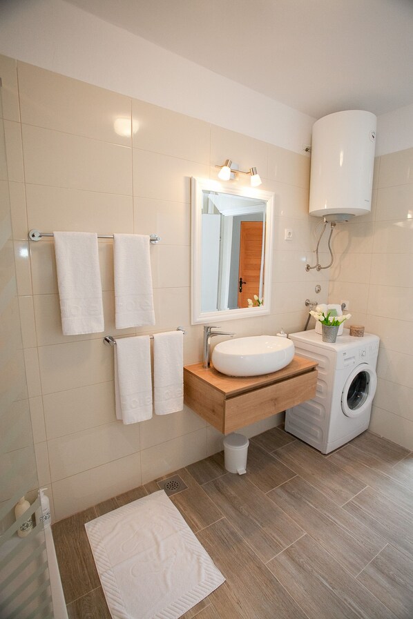 A modern bathroom with a sink, mirror, towel rack, and a washing machine.