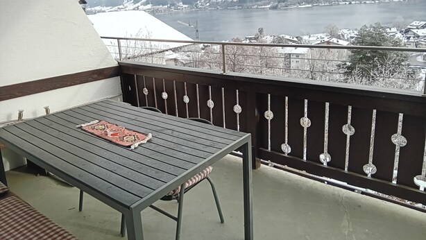 Een balkon met een tafel en stoelen, met uitzicht op een meer en besneeuwde bergen.