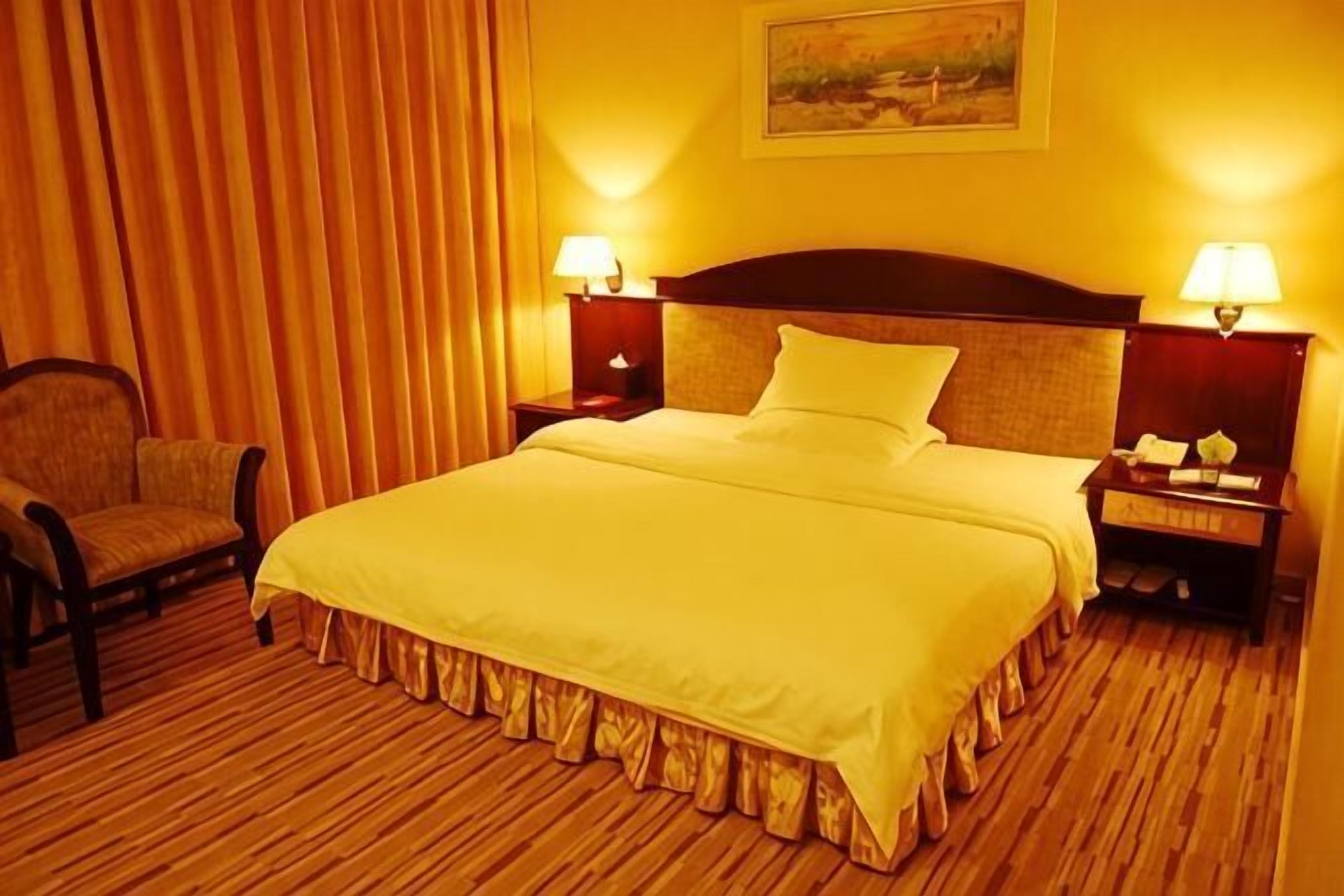 Quarto de hotel com uma cama grande, duas mesas de cabeceira com luminárias, uma cadeira e um quadro na parede.