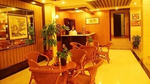 Un vestíbulo de hotel con mobiliario de mimbre, una recepción y plantas en macetas.