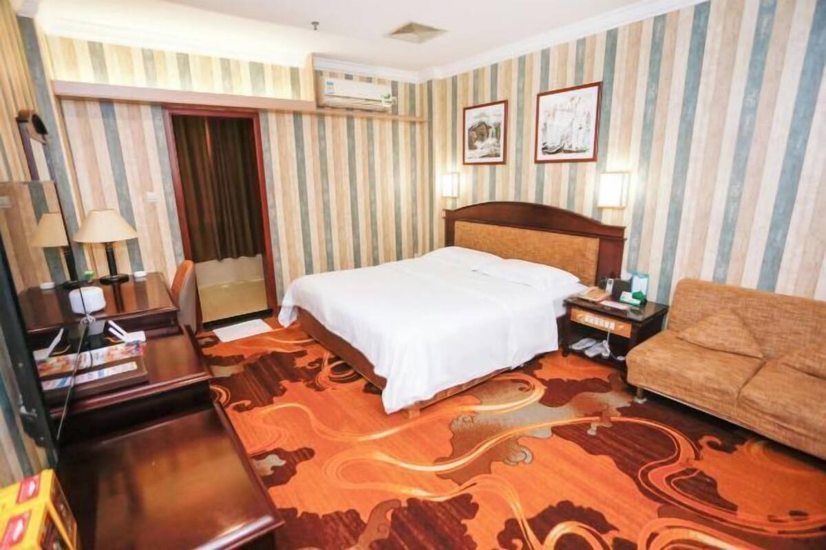 Een hotelkamer met een bed, een slaapbank, een bureau met een lamp, een nachtkastje en gestreept behang.