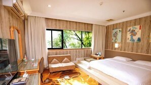 Habitación de hotel con cama, escritorio con computadora, una silla, sofá, televisor y ventana con vista a árboles.