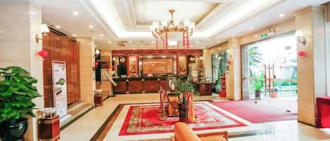 A hotel lobby with a reception desk, seating area, and a chandelier.