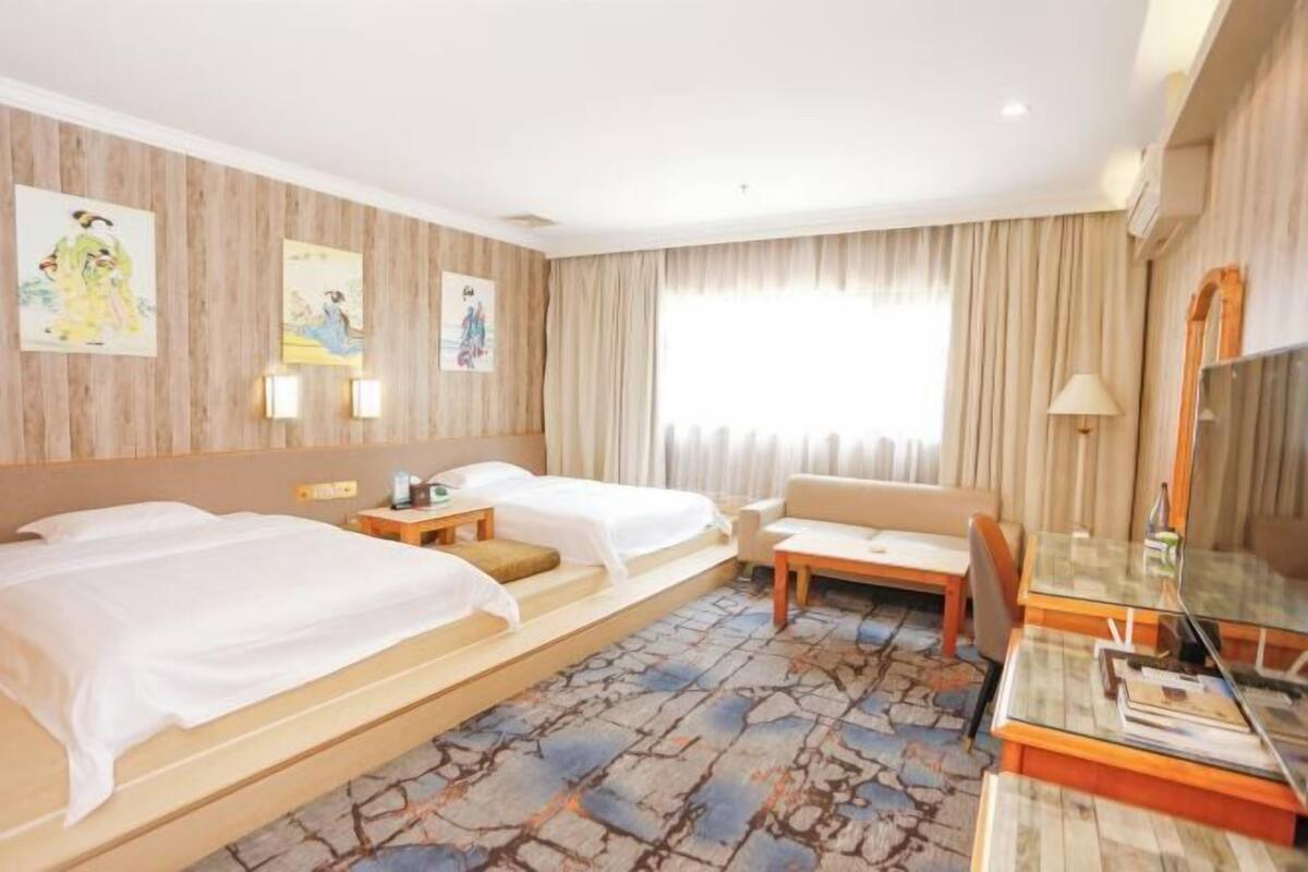 Een hotelkamer met twee bedden, een sofa, een bureau en een televisie.