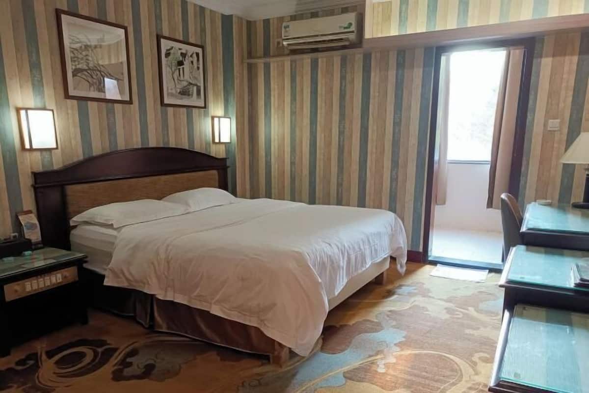 Een hotelkamer met een bed, een nachtkastje, een bureau met stoel en een raam met gordijnen.