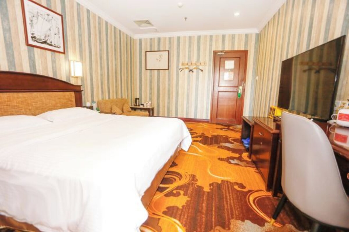 Una habitación de hotel con una cama, un escritorio, una silla, un televisor y una puerta.
