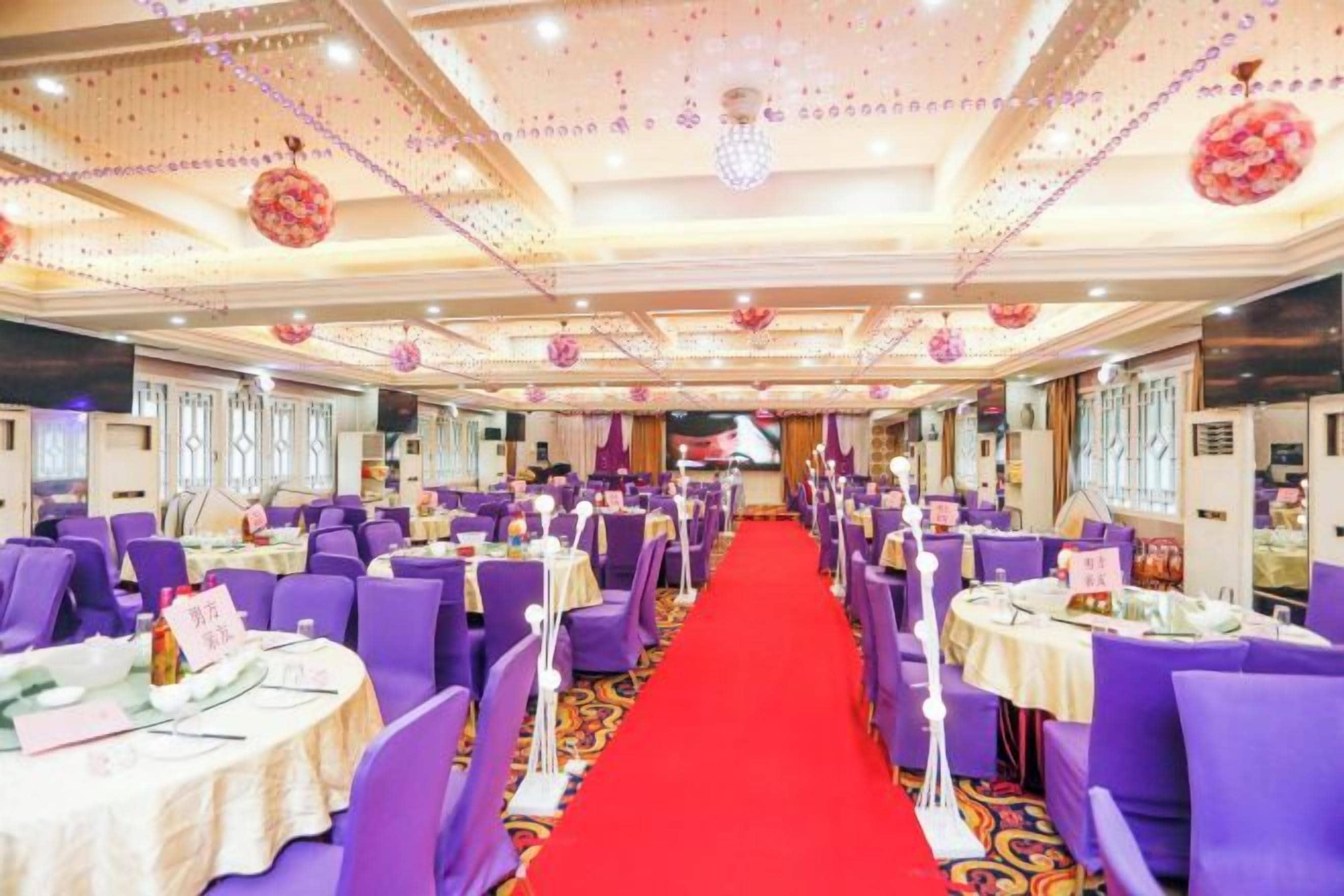 A banquet hall with round tables, purple chairs, and a red carpet.